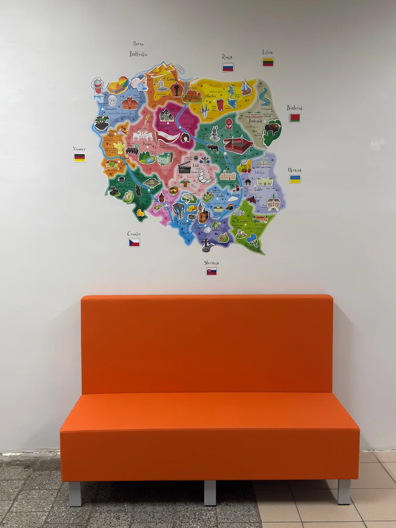 Kolorowa mapa Polski z regionami i flagami sąsiednich krajów wydrukowana na ścianie nad pomarańczową ławką w szkole